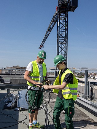 Climtech Techniker Dach Foto von zwei Personen in Schutzkleidung auf einem Dach, die ein Kabel sortieren
