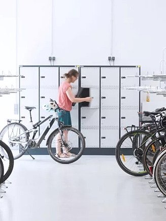 Picture of a woman standing next to her bicycle in a bicycle cellar and opening a locker