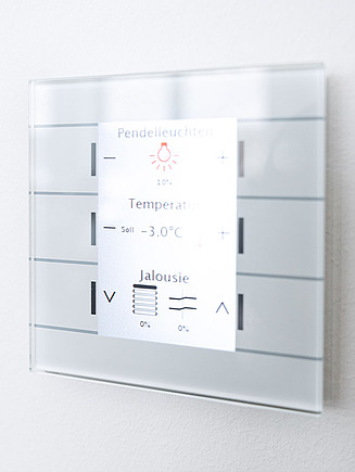 Picture of a control unit with the option of controlling light, temperature and blinds, hanging on a wall.