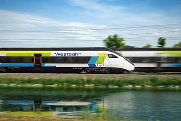Picture of a train passing another train quickly, reflected in the water in the foreground