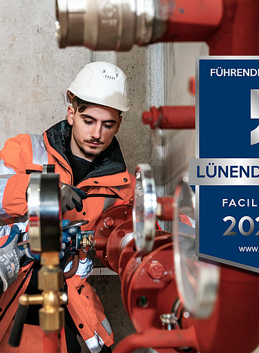 Fotomontage von dem Lünendonk 2026-Siegel auf einem Bild von zwei Männern in Arbeitskleidung, die an einem roten Rohr arbeiten