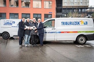 STRABAG PFS Triburuzek Foto von vier Männern, die sich vor einem Gebäude und zwei Autos einen großen Schlüssel übergeben