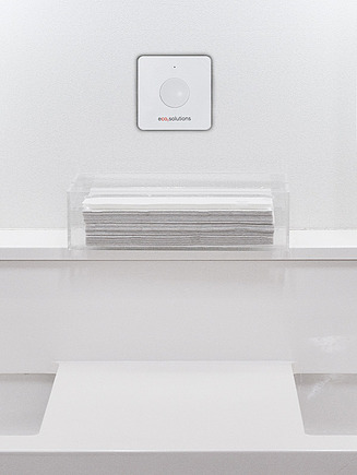 Bild eines Doppelwaschbeckens, in der Mitte hängt ein weißer Kasten mit einer Taste an der Wand