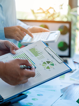 Image of several people evaluating charts and reports with green graphs and a calculator;