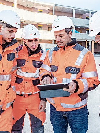Photo of four people in protective clothing looking at something on a tablet outside
