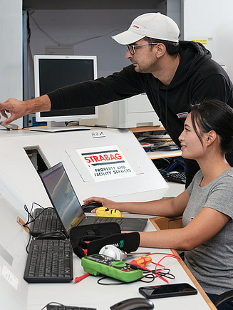 Photo of two employees at a table with monitors and a laptop top