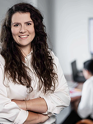 Im Vordergrund lächelnde weibliche Person, im Hintergrund zwei unscharfe Personen