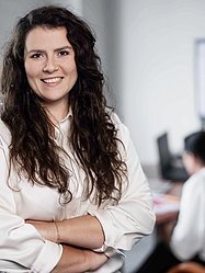 Im Vordergrund lächelnde weibliche Person, im Hintergrund zwei unscharfe Personen