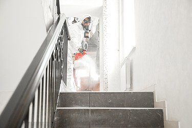 Obrázek osoby v ochranném obleku při dezinfekci