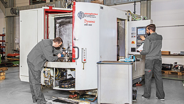 Zwei Personen führen Bedien- und Wartungsarbeiten an einer großen Fräsmaschine durch