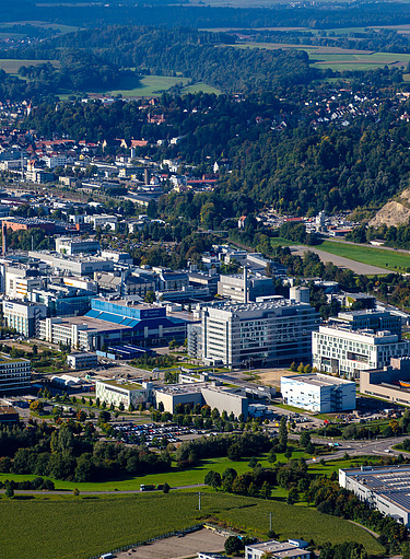 Luftaufnahme einer Stadt und eines Gebäudekomplexes, umgeben von Grünanlagen und Wald