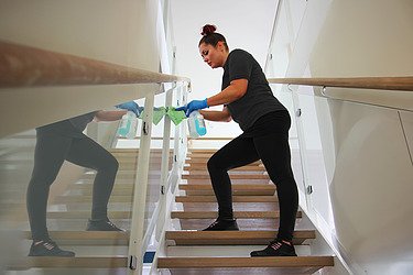 Obrázek ženy, která uklízí budovu a čistí zábradlí hadříkem