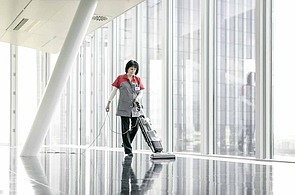 Photo of a cleaner at a floor mopping machine in a large bright room