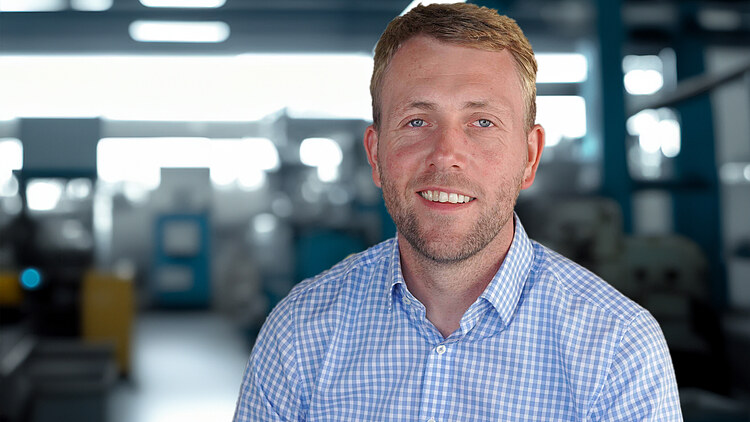 Photo of a man in a shirt in front of a blurred storage room