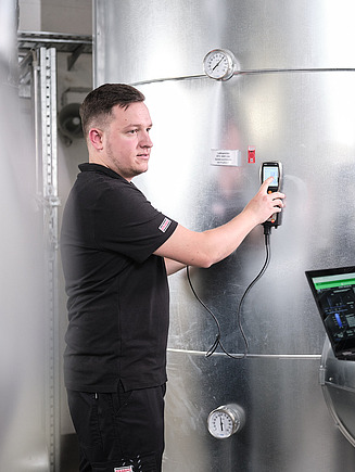 Photo of two people taking a measurement on a boiler and analyzing it on a notebook