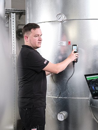 Foto von zwei Personen, die eine Messung an einem Kessel durchführen und es auf einem Notebook analysieren