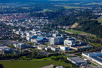 Luftaufnahme einer Stadt und eines Gebäudekomplexes, umgeben von Grünanlagen und Wald