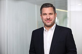 Direktionsleiter Tobias Hamberger im Anzug vor einer Glaswand