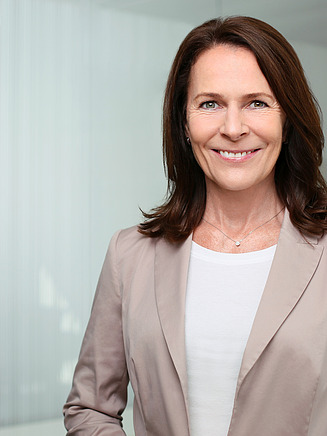 Foto von einer lächelnden Frau im Blazer vor einer Glasscheibe