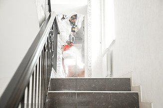 Schädlingsbekämpfung Bild einer Person im Schutzanzug, die in einem Treppenhaus Schädlingsbekämpfung durchführt