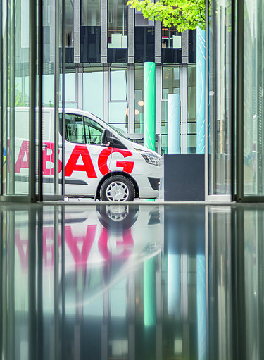 STRABAG-Lieferwagen vor modernem Bürogebäude, aufgenommen durch eine reflektierende Glasfassade.