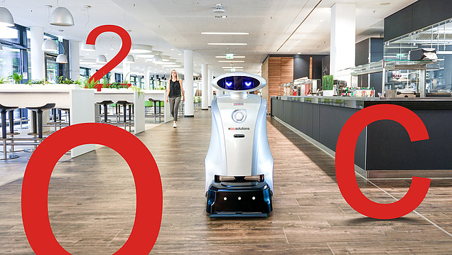 Bild von einem Reinigungsroboter in einer Kantine für den Einsatz automatisierter und hygienischer Reinigung. Weiterhin sind große rote Aufsteller von C, O und 2 zu sehen.