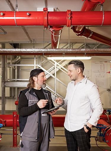 Obrázek dvou zaměstnanců společnosti STRABAG Property and Facility Services ve sklepní místnosti s řídicím centrem sprinklerů