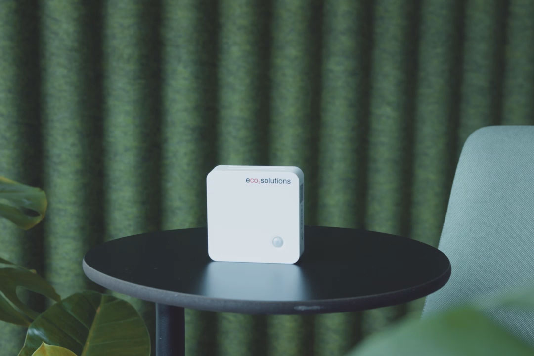 Bild von einem eco2state Sensor, welcher auf einem runden Tisch vor grünem Hintergrund steht.