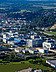 Luftaufnahme einer Stadt und eines Gebäudekomplexes, umgeben von Grünanlagen und Wald