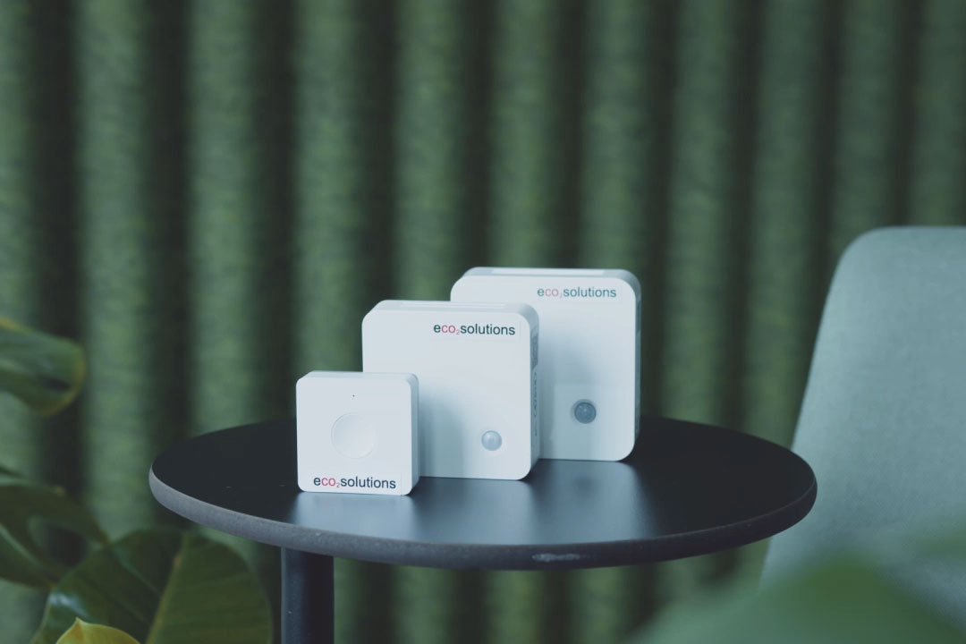 Obrázek tří senzorů eco2state různých velikostí stojících na kulatém stole na zeleném pozadí. 