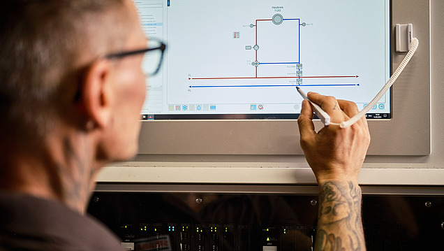 Foto von Mitarbeiter, der vorbereitend für eine Wartung ein Touchscreen-Display mit einem technischen Diagramm bedietn