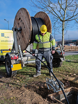 Photo of a person in protective clothing laying a cable from a drum into the ground