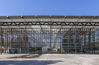 Photo of a large building made of glass and steel girders with a large concrete forecourt